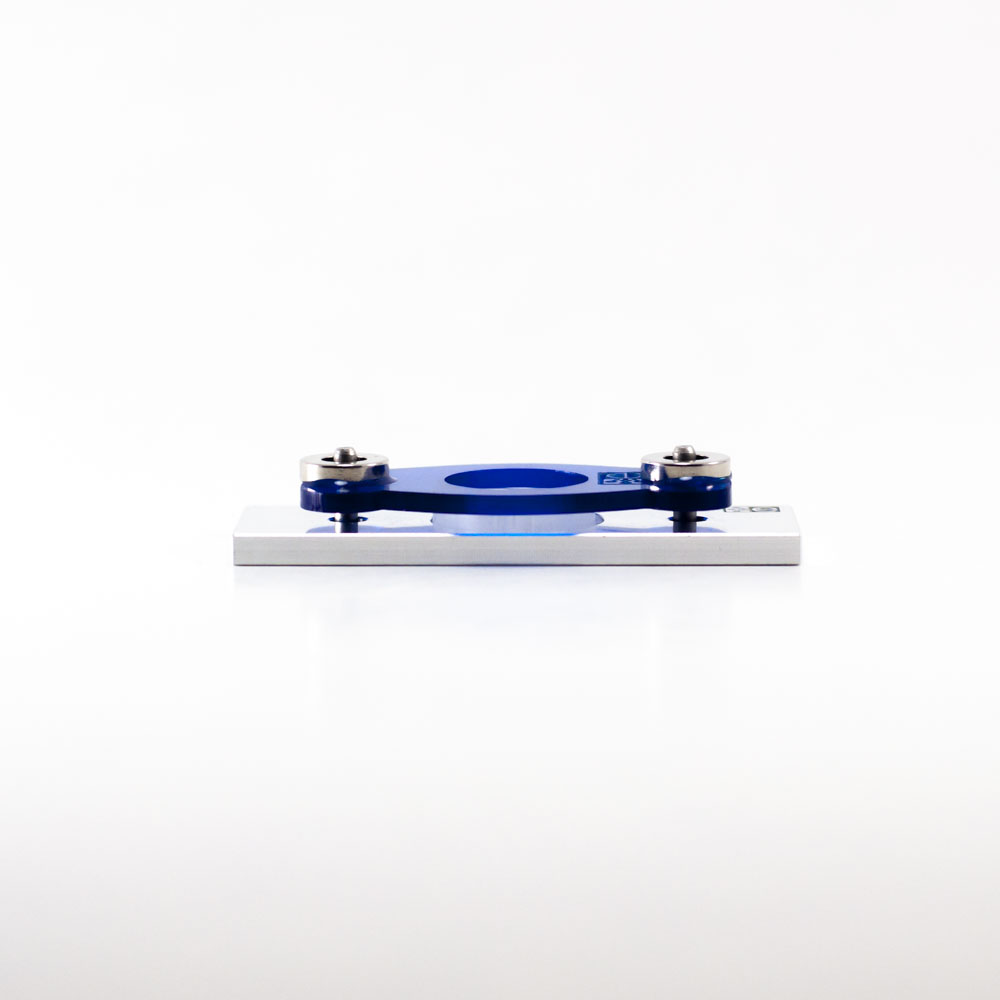 Photograph. Sideview of microscopy adapter made from aluminum, rectangular shape with two pins protruding upwards, engraved eNUVIO logo on top right, a round Omega device is placed in the middle, blue acrylic plate attached to pins and placed on top of OMEGA device