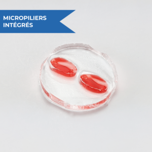Photographie du dispositif OMEGA-MP, disque en PDMS avec deux chambres musculaires ovales contenant chacune deux micropiliers intégrés pour la formation de tissu musculaire en 3D, rempli de liquide rouge.